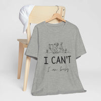 I Can’t, I’m Busy Unisex Jersey Short Sleeve TeeShow off your love for quiet moments with our I Can’t, I’m Busy Unisex Jersey Short Sleeve Tee. Perfect for book lovers and those who cherish their downtime, this tee features a playful illustration of a per