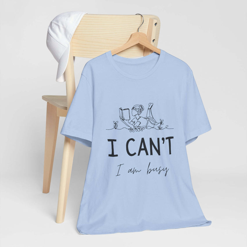 I Can’t, I’m Busy Unisex Jersey Short Sleeve TeeShow off your love for quiet moments with our I Can’t, I’m Busy Unisex Jersey Short Sleeve Tee. Perfect for book lovers and those who cherish their downtime, this tee features a playful illustration of a per