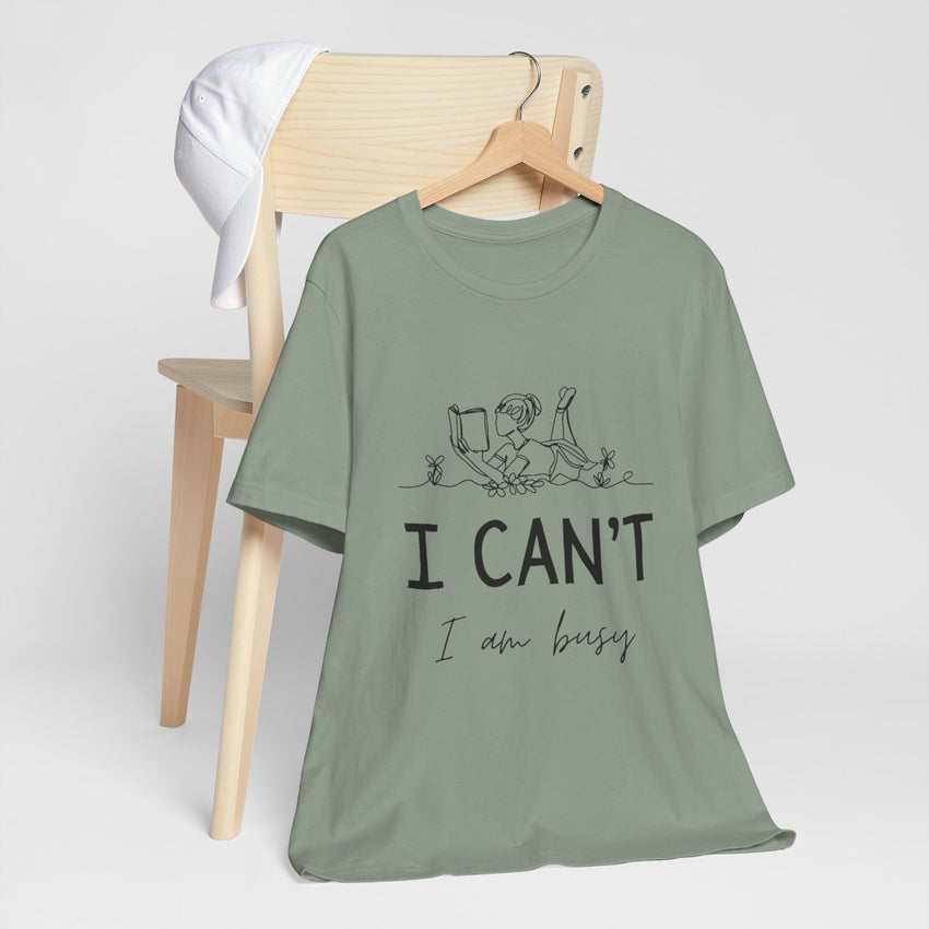 I Can’t, I’m Busy Unisex Jersey Short Sleeve TeeShow off your love for quiet moments with our I Can’t, I’m Busy Unisex Jersey Short Sleeve Tee. Perfect for book lovers and those who cherish their downtime, this tee features a playful illustration of a per